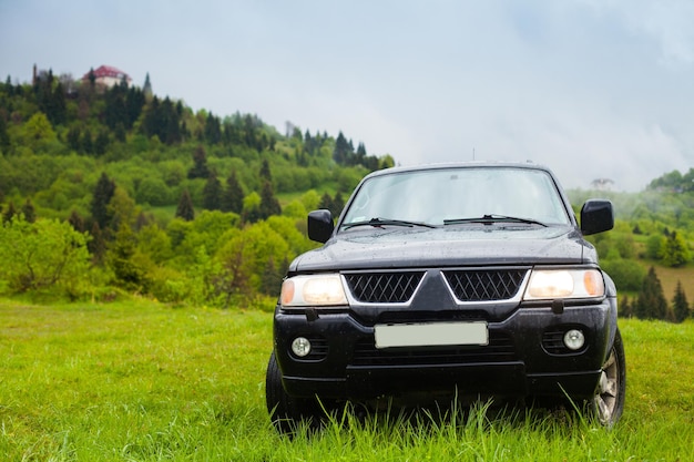 Foto vista superior del coche negro de pie entre la naturaleza del verano. la casa está de pie en la cima de la colina en el fondo.