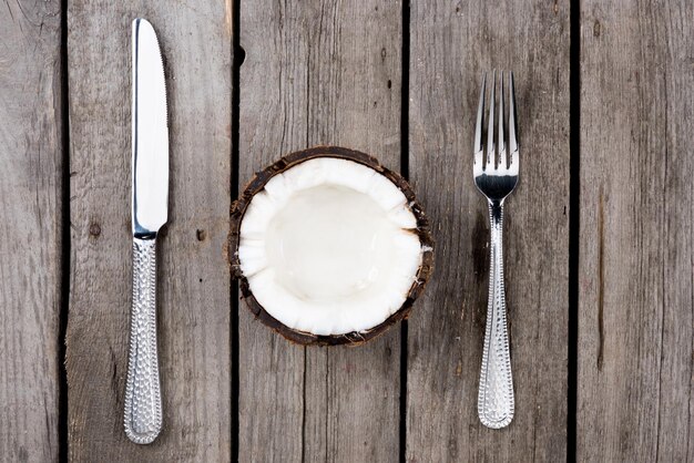 Vista superior de coco a la mitad con tenedor y cuchillo en la mesa de madera