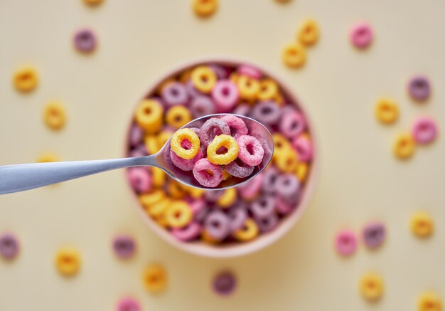 Vista superior de coloridos bucles de cereales de frutas en un tazón y una cuchara en primer plano sobre fondo claro