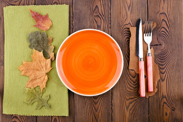 Vista superior com prato laranja vazio pronto para colocar talheres de comida folhas coloridas na mesa de madeira rústica Mesa de outono com espaço de cópia