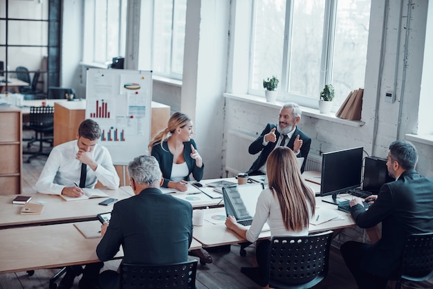 Vista superior de compañeros de trabajo discutiendo el próximo paso comercial mientras trabajan junto con colegas en la oficina moderna