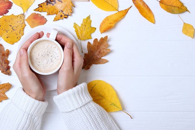 Vista superior de la composición de otoño taza de café en las manos y hojas de otoño