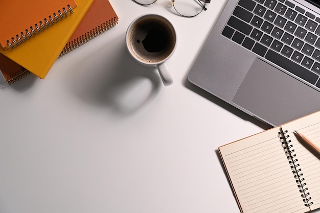 Vista superior de la computadora portátil, anteojos y taza de café en la mesa blanca