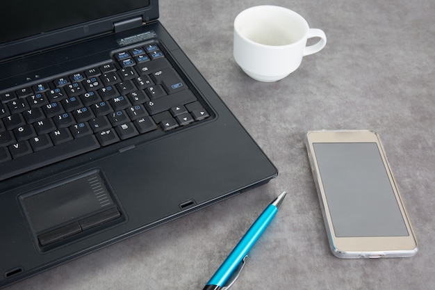 Vista superior de la computadora portátil, teléfono celular con pantalla en blanco, taza de café, bolígrafo