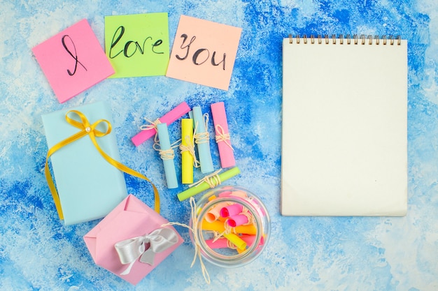 Foto vista superior del concepto del día de san valentín te amo escrito en notas adhesivas de colores cuaderno de desplazamiento deseos papeles en tarro regalos en la mesa