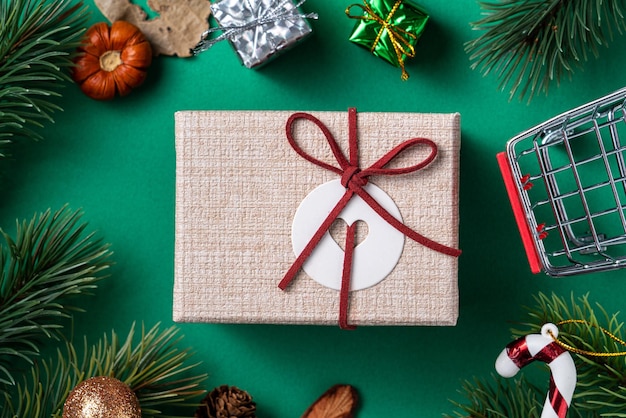 Vista superior del concepto de diseño de compras navideñas con caja de regalo y carrito de compras en el fondo de la mesa verde