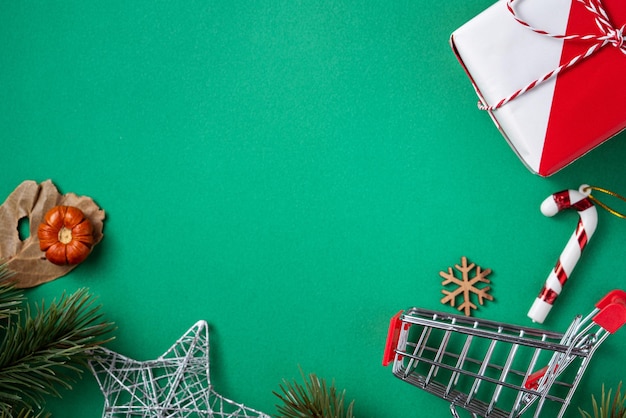 Vista superior del concepto de diseño de compras navideñas con caja de regalo y carrito de compras en el fondo de la mesa verde