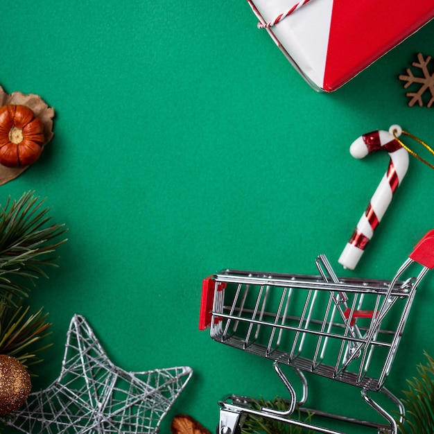 Vista superior del concepto de diseño de compras navideñas con caja de regalo y carrito de compras en el fondo de la mesa verde