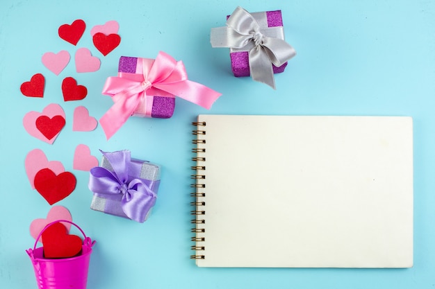 Vista superior del concepto de febrero pegatinas de corazón rojo y rosa esparcidas desde el mini cuaderno de regalos de cubo en el cuadro azul