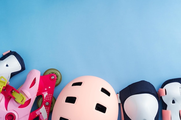 Foto vista superior del conjunto de equipo de protección de patines, rodilleras, coderas y muñequeras y casco en colores rosas fondo azul plano