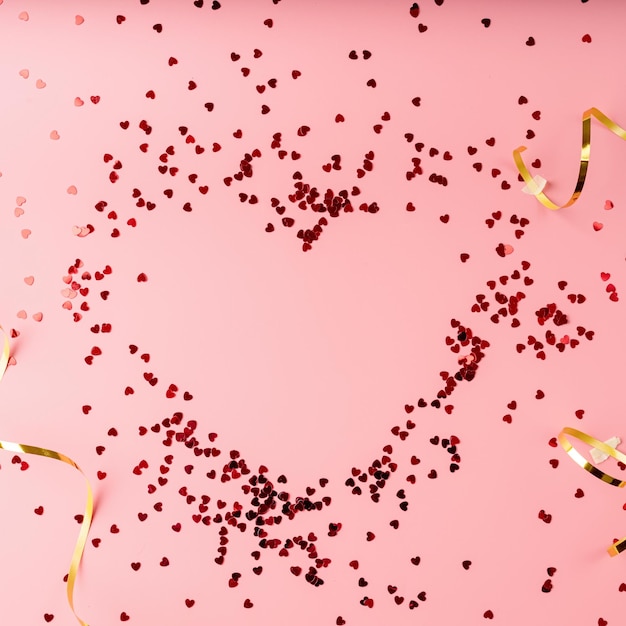 Vista superior del corazón de confeti en forma de corazón rojo plano yacía sobre fondo rosa