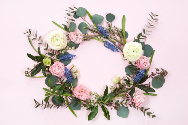 Foto vista superior de la corona de flores de marco redondo con rosas, ranúnculos, hojas, brotes, ramas aisladas sobre fondo blanco.