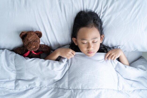 Vista superior criança menina asiática dorme na cama com um ursinho de brinquedo