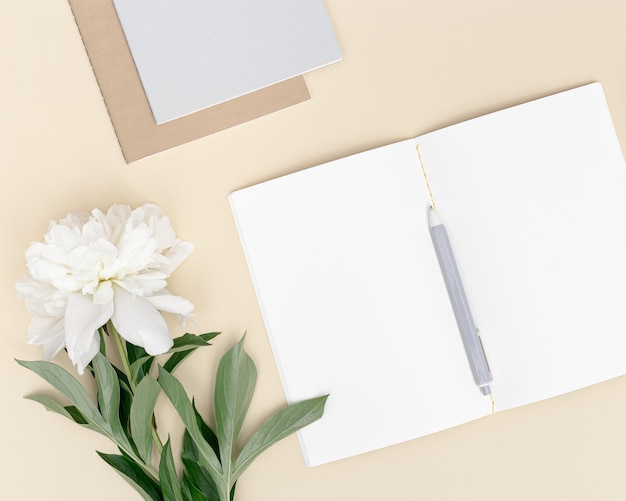 Vista superior del cuaderno abierto con páginas en blanco y flor de peonía blanca en la mesa Espacio de trabajo creativo