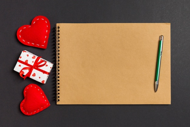 Vista superior del cuaderno artesanal rodeado de corazones y cajas de regalo en la mesa. Día de San Valentín