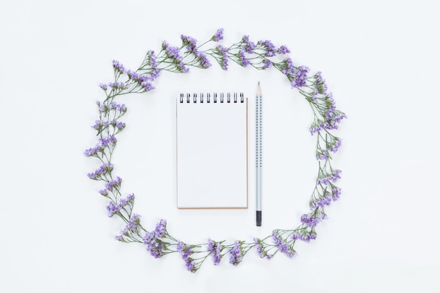 Vista superior del cuaderno en blanco con lápiz en marco floral de flor