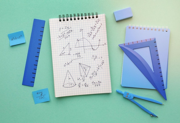 Vista superior de un cuaderno con ecuaciones matemáticas escritas en él y artículos estacionarios azules