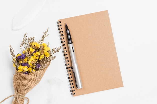 Vista superior del cuaderno espiral de la escuela con pluma y flores estáticas sobre fondo blanco