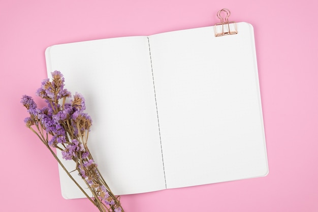Vista superior del cuaderno y flor violeta en rosa