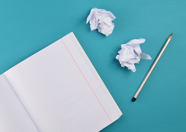 Vista superior del cuaderno con lápiz y bola de papel arrugado blanco sobre fondo azul.