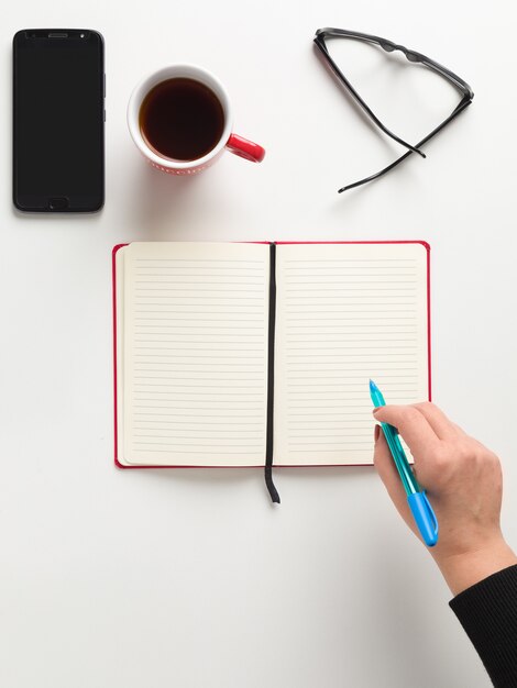 Vista superior de un cuaderno rojo abierto, una mano femenina con un bolígrafo azul