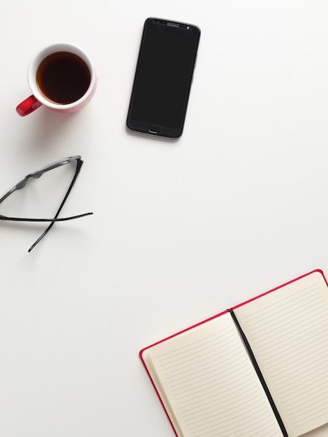 Vista superior de un cuaderno rojo abierto, una taza de café roja, un teléfono celular y gafas