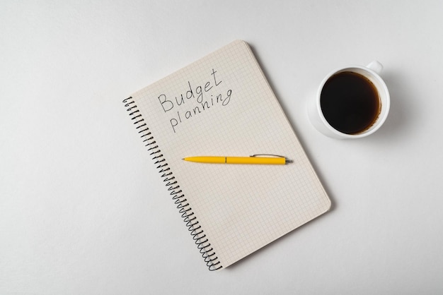Vista superior del cuaderno con texto de planificación presupuestaria Planificación de boda Bloc de notas y café sobre fondo blanco