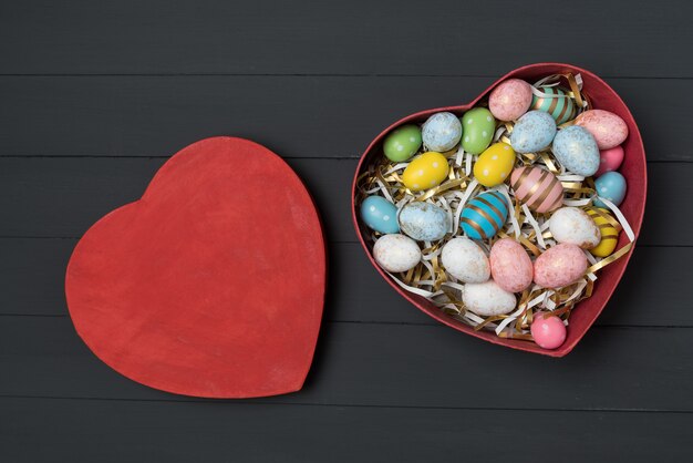 Vista superior del cuadro rojo en forma de corazón con coloridos huevos de Pascua. Fondo negro. Felices Pascuas