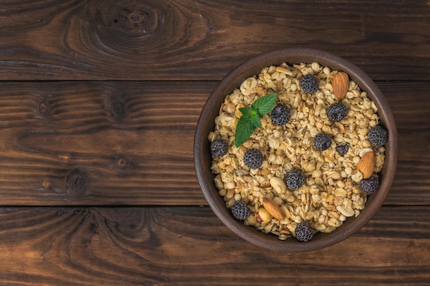 Vista superior de un cuenco de arcilla con bayas de granola y almendras sobre una mesa rústica