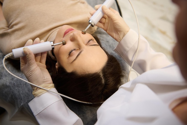 Vista superior da bela mulher no spa recebendo tratamento profissional de cuidados com a pele e rejuvenescimento com pulsos elétricos no rosto terapia antienvelhecimento microcorrente em uma clínica de cosmetologia