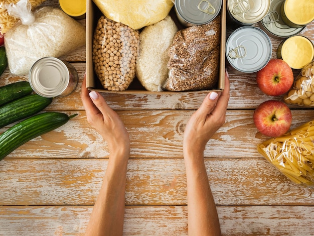 Vista superior da caixa com comida para doação e mãos