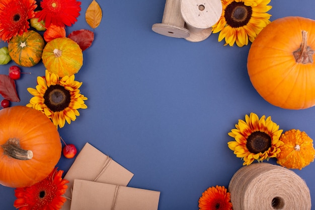 Vista superior da caixa de presente de artesanato com flores amarelas e laranja, carretel de corda e abóboras na parede azul Cartão em branco para o projeto de trabalhos criativos. configuração plana