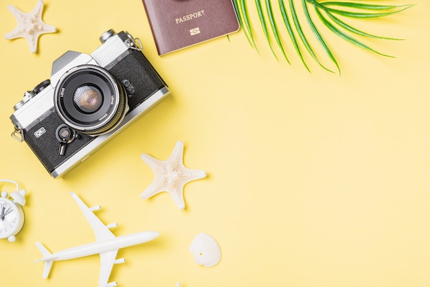 Vista superior da câmera retro, avião de brinquedo, passaporte, estrelas do mar e despertador na superfície amarela