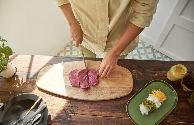 Vista superior da chef profissional cortando carne com faca no processo de cozinhar bife tártaro na cozinha em casa