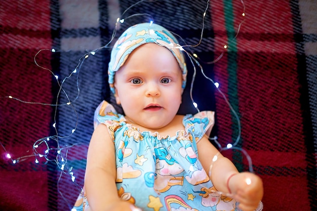 Vista superior da linda menina de pijama brincando com luzes de natal enquanto estava deitado na manta quadriculada