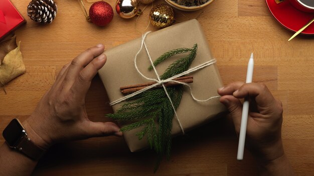 Vista superior da mão masculina abrindo uma caixa de presente na mesa de madeira com enfeites de natal