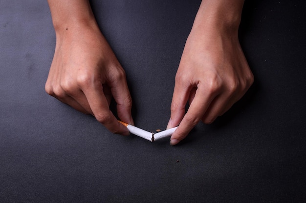 Vista superior da mão segurando cigarros quebrados em fundo de cor preta Cuidados de saúde e parar de fumar c