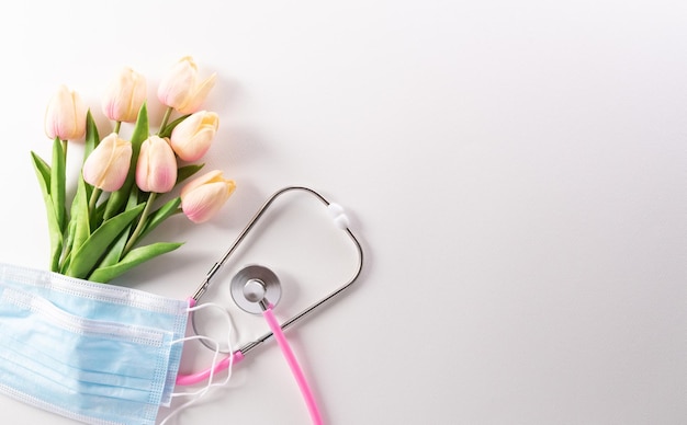 Vista superior da máscara médica do estetoscópio médico e flores no fundo branco dia internacional da enfermeira e conceito médico