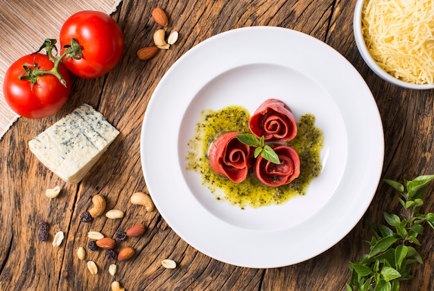 Vista superior da massa em forma de rosa com tomate, queijo, manjericão e molho pesto na mesa de madeira