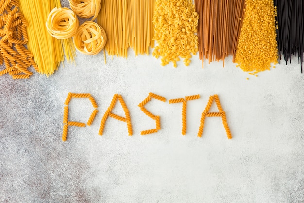 Vista superior da massa italiana crua com espaço da cópia no fundo branco do cocnrete. Postura plana de comida italiana