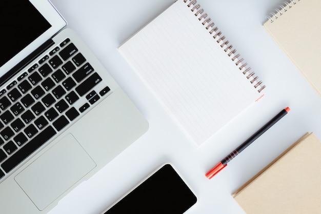 Vista superior da mesa de escritório branca com computador portátil, smartphone, caderno e uma caneta para o conceito de negócios e espaço de trabalho