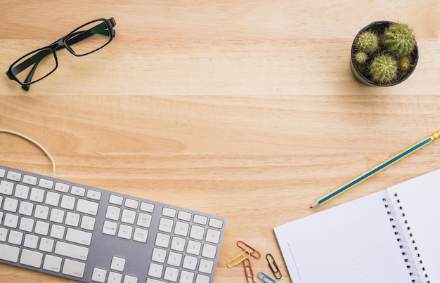 Vista superior da mesa de escritório com teclado de computador, óculos, caderno e cacto