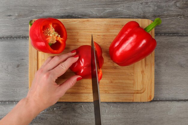 Vista superior da mesa, mulher cortando pimentão vermelho com faca de chef na tábua.