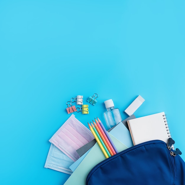 Vista superior da mochila azul com artigos de papelaria da escola sobre o fundo da mesa azul, de volta ao conceito de design da escola.