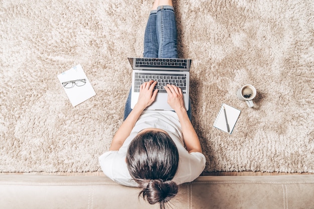 Vista superior da mulher com o laptop sentado no chão em casa.