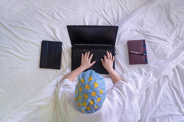 Vista superior da mulher de roupão branco com touca de banho usando laptop enquanto estava deitado na cama