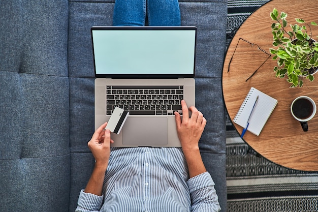 Vista superior da mulher segurando um cartão de crédito e compras on-line em um computador.