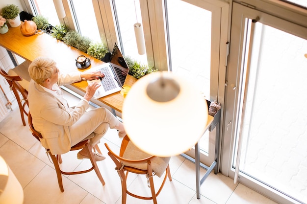 Vista superior da mulher sênior trabalhando no laptop e tomando café no café