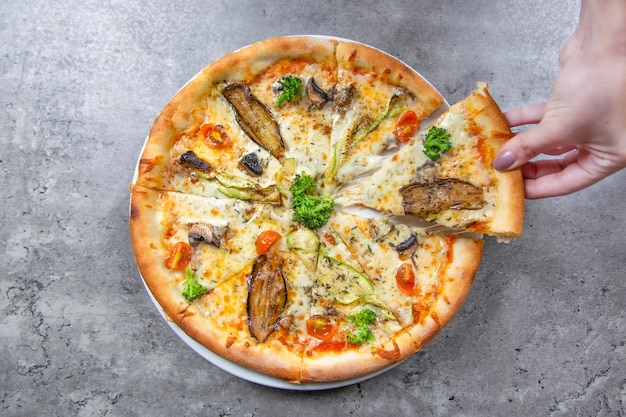 Vista superior da pizza com legumes e uma mulher pega um pedaço