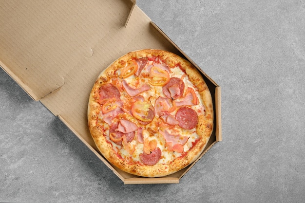 Vista superior da pizza com linguiça curada de presunto e fatias de tomate em caixa de papelão